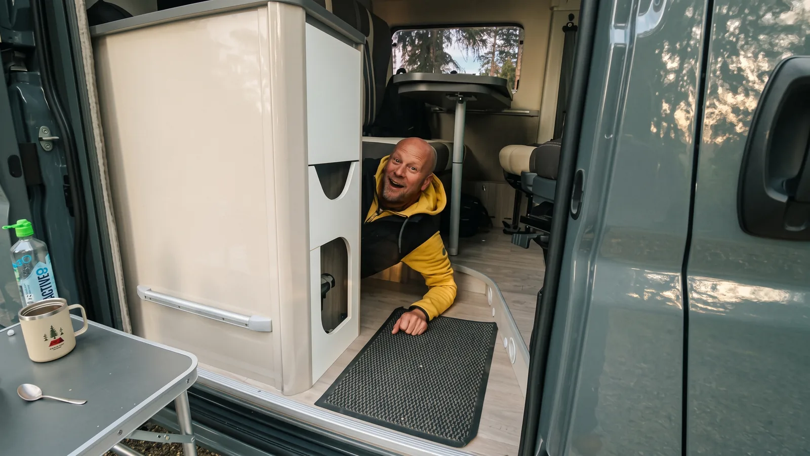 Blick durch die Schiebetür in den Camper: Eric schaut hinter dem Küchenblock hervor